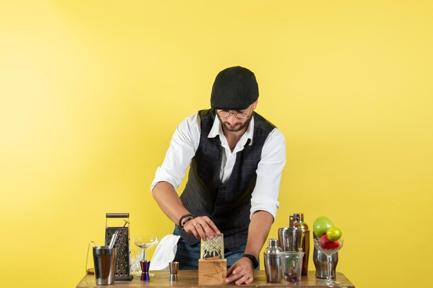 Front view male bartender in front of table with shakers preparing drink on yellow wall bar alcohol night youth drink club