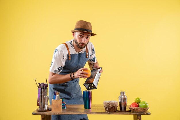 Front view male bartender preparing a drink on yellow wall club night bar alcohol drink job color