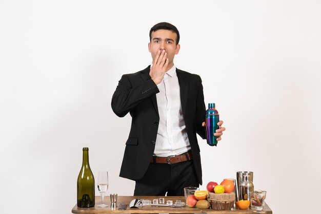 Front view male bartender standing in front of table with drinks and shakers on white wall night drinks club alcohol bar male