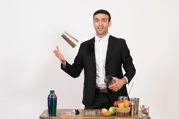 Front view male bartender in suit working with shakers and making drink on white wall night dance drink male bar club