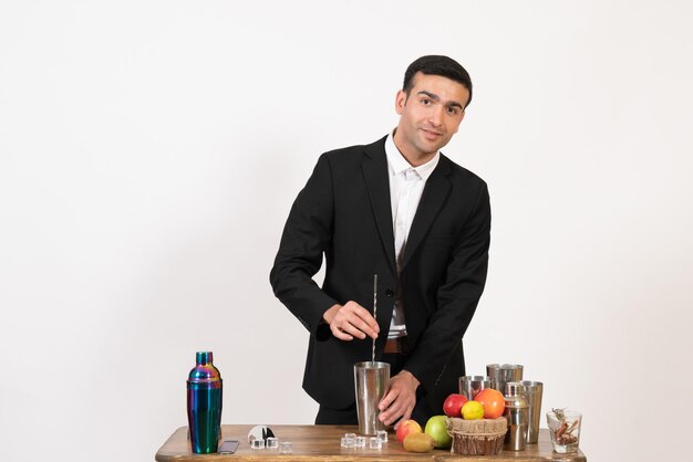 Front view male bartender in suit working with shakers and making drink on a white wall night drink bar club male dance