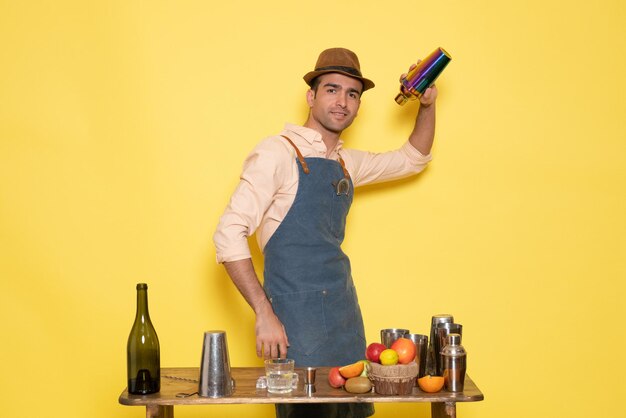 シェーカーで作業し、黄色の壁で飲み物を作る正面図の男性バーテンダーナイトドリンクアルコールバークラブ男性