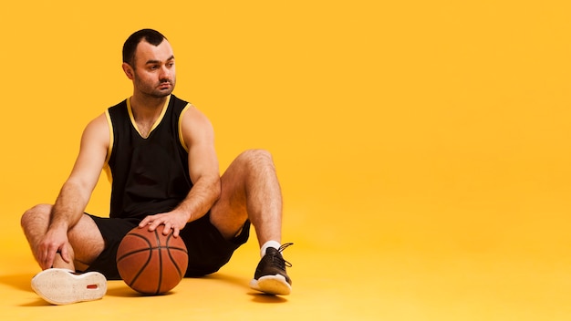 Front view of male basketball player sitting down with ball and copy space