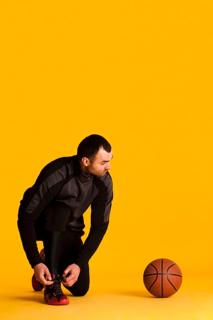 ボールとコピースペースで靴ひもを結ぶ男性のバスケットボール選手の正面図