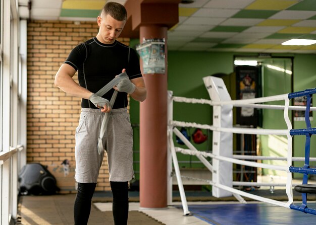 Вид спереди мужчины-боксера, оборачивающего руки перед тренировкой на боксерском ринге