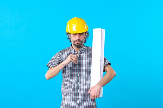 Front view male builder in helmet holding plan on blue