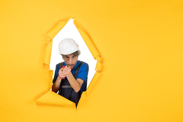 Front view male builder holding drill on yellow background