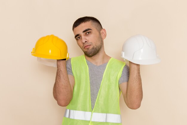 Free photo front view male builder holding helmets on light background