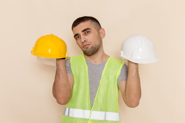 Front view male builder holding helmets on light background