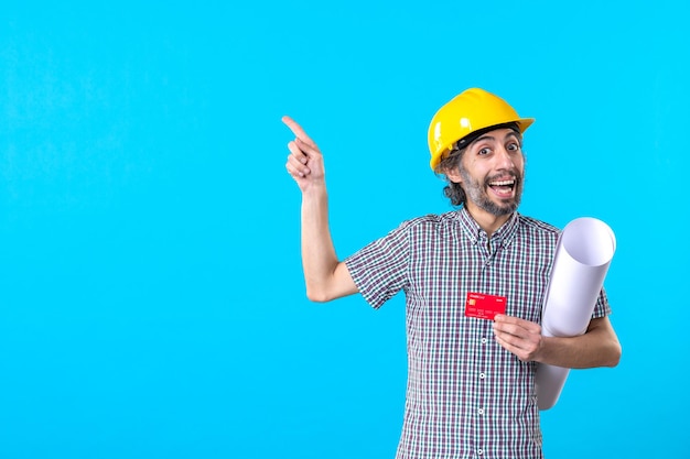 Front view male builder holding plan and bank card on a blue background color constructor job architecture money building