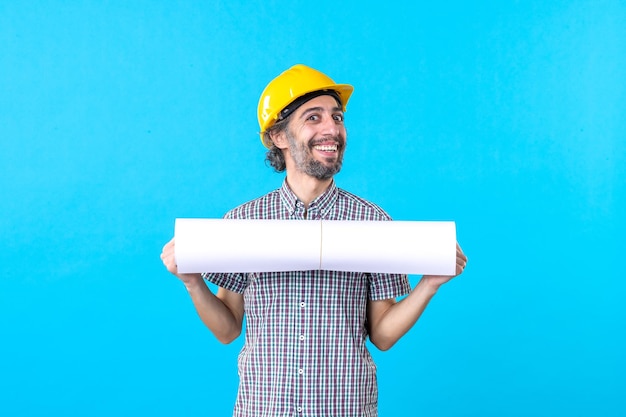 Vista frontale del costruttore maschio che tiene il piano su uno sfondo blu lavoro di costruzione ingegnere architettura costruttore di grattacieli