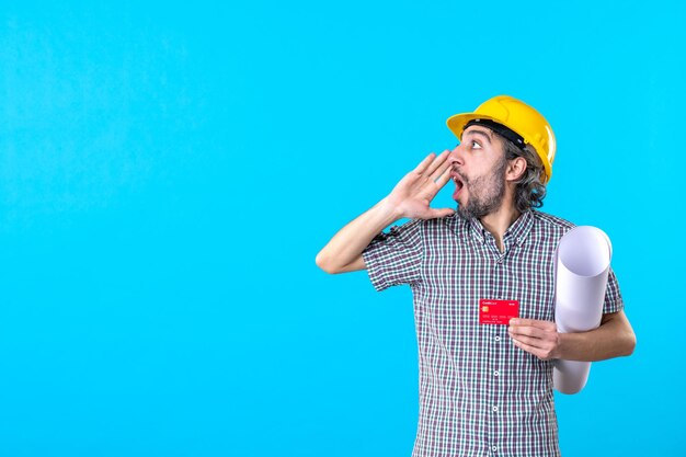 Front view male builder holding plan and red bank card on a blue background color money design constructor job work architecture building