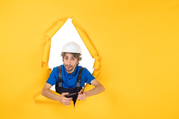 Front view male builder holding pliers on a yellow background