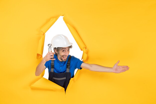 front view male builder holding pliers on yellow background