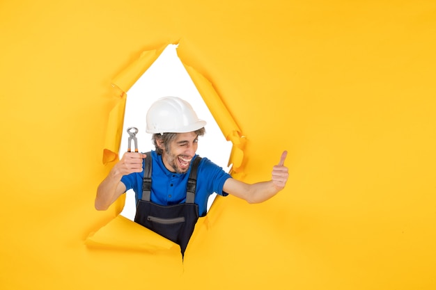 Front view male builder holding pliers on yellow background