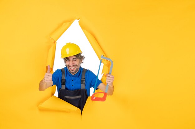 Бесплатное фото Строитель-мужчина в униформе, держащий луковую пилу на желтом фоне, вид спереди