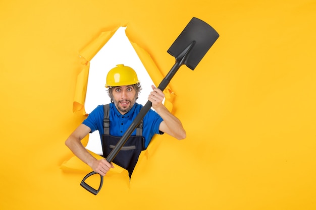 Вид спереди мужчина-строитель в форме, держащий лопату на желтом фоне
