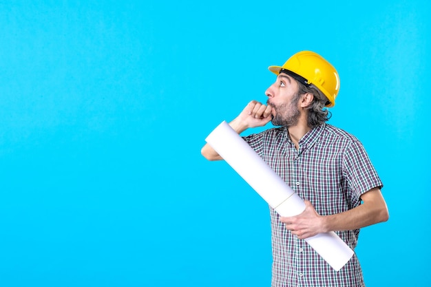Бесплатное фото Вид спереди мужчина-строитель в желтом шлеме с планом на синем фоне, архитектура здания, конструктор, цвет, собственность, рабочий, инженер