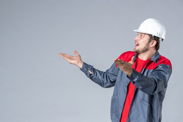 front view male builder in uniform and helmet on gray background