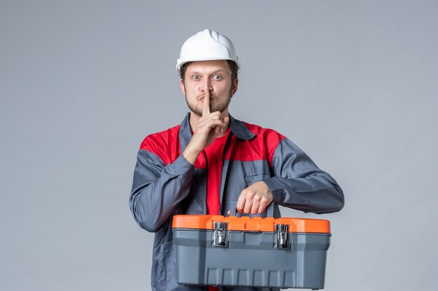 front view male builder in uniform and helmet holding tool case on gray background