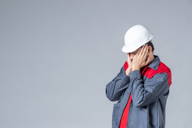 front view male builder in uniform and helmet stressed on gray background