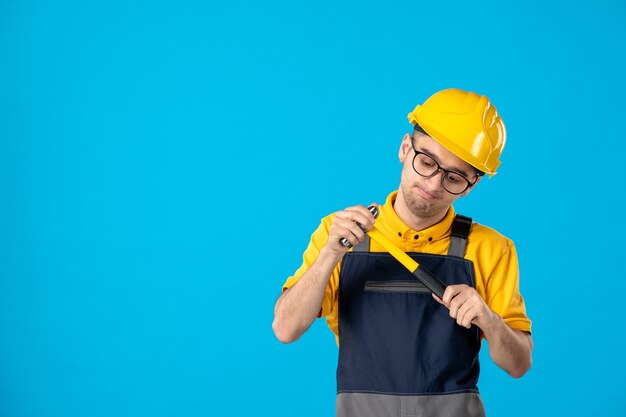 Front view of male builder in uniform and helmet with hammer on blue wall