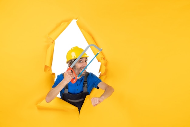 Free photo front view male builder in uniform holding bowsaw on a yellow background