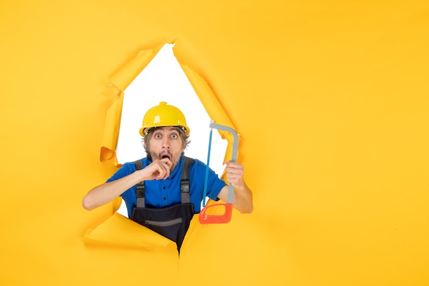 Front view male builder in uniform holding bowsaw on the yellow background