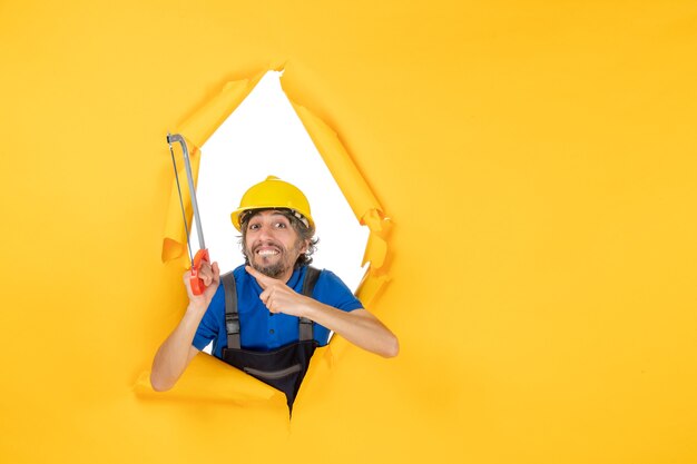 Front view male builder in uniform holding bowsaw on the yellow background