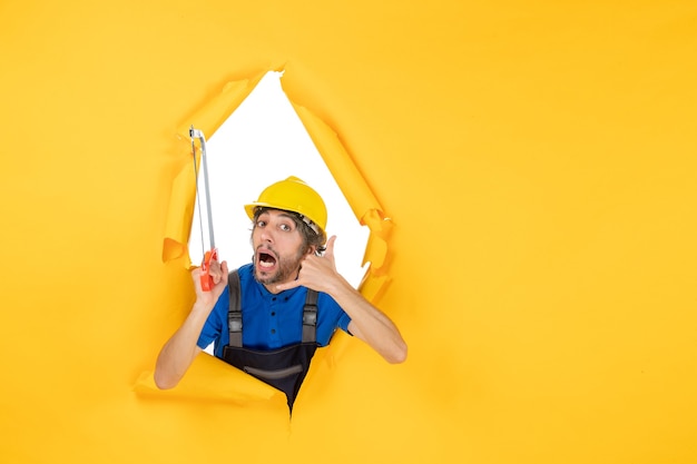 Front view male builder in uniform holding bowsaw on yellow background