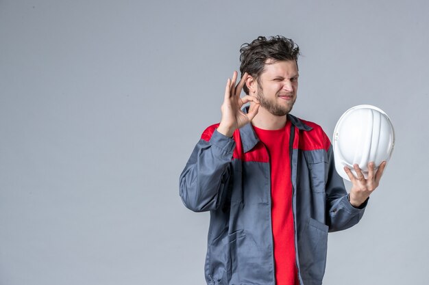 front view male builder in uniform holding helmet on light background