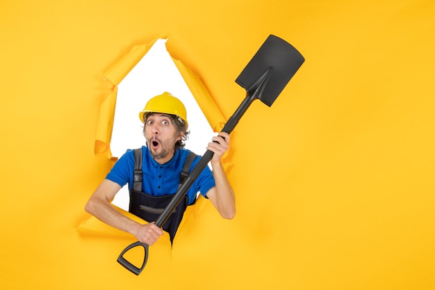 Front view male builder in uniform holding shovel on light yellow background