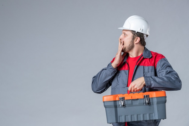 front view male builder in uniform holding tool case on gray background