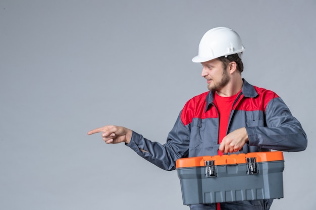 front view male builder in uniform holding tool case on gray background