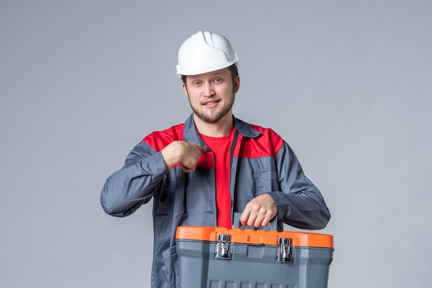 front view male builder in uniform holding tool case on gray background