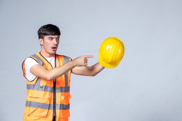 front view of male builder in uniform holding yellow helmet on white wall