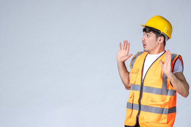 front view of male builder in uniform talking to someone on white wall