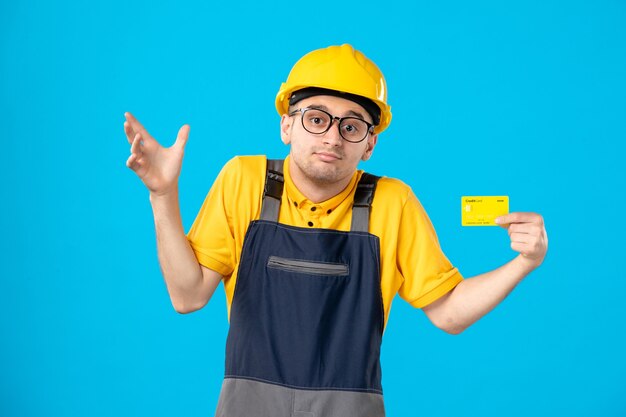 Front view of male builder in uniform with credit card on blue wall