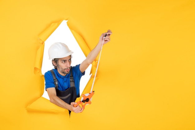 Foto gratuita costruttore maschio di vista frontale in uniforme con il dispositivo sul costruttore di edifici di architettura del lavoratore di colore della parete gialla