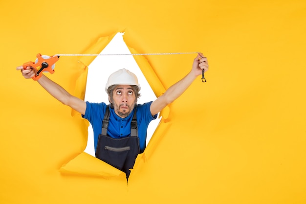 Foto gratuita costruttore maschio di vista frontale in uniforme con il dispositivo su un lavoro di costruttore dell'operaio di costruzione di architettura di colore del lavoro della parete gialla