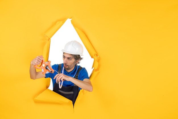 Мужчина-строитель в униформе с устройством на желтой стене, вид спереди, цветная архитектура, строительный рабочий, конструктор