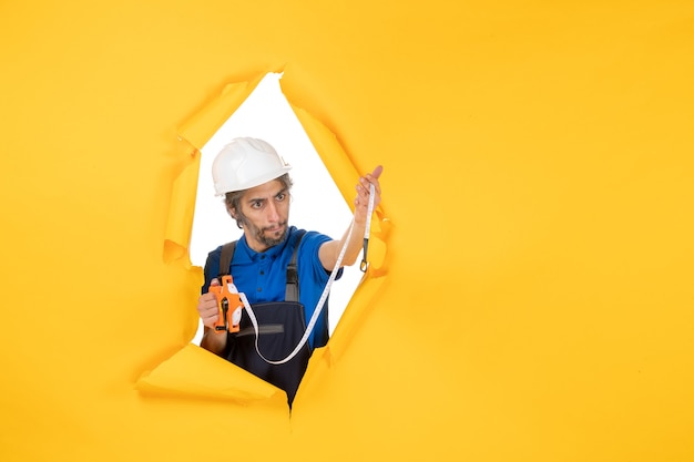 Вид спереди мужчина-строитель в униформе с устройством на желтой стене работает цветная архитектура здания рабочий конструктор