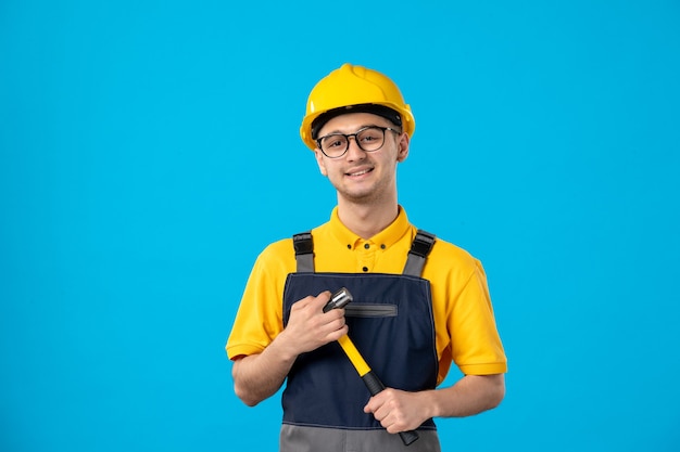 Вид спереди мужчины-строителя в униформе с молотком в руках на синей стене