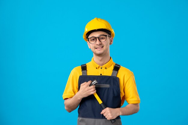 Front view of male builder in uniform with hammer in his hands on a blue wall