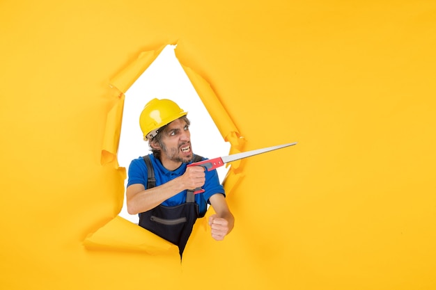 Front view male builder in uniform with instrument in his hands on yellow wall building color constructor work worker job