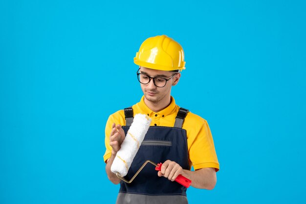 Front view of male builder in uniform with paint roller in his hands on a blue wall