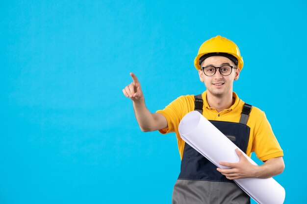 Front view of male builder in uniform with paper plan on blue wall