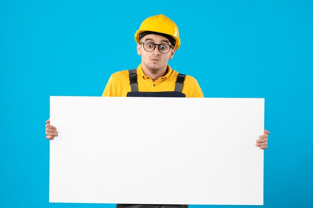 Вид спереди мужчины-строителя в форме с бумажным планом на синей стене