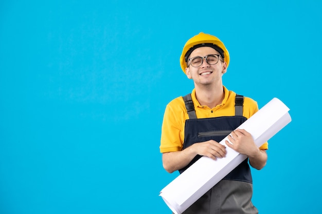 Front view male builder in uniform with paper plan on blue 