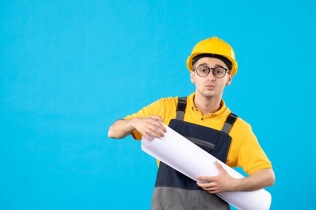 Front view male builder in uniform with paper plan on blue 